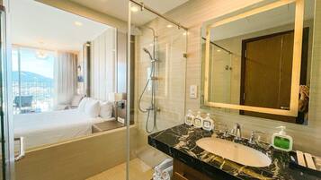 A hotel bathroom with a large mirror, a bathtub, a shower, and a sink with toiletries.