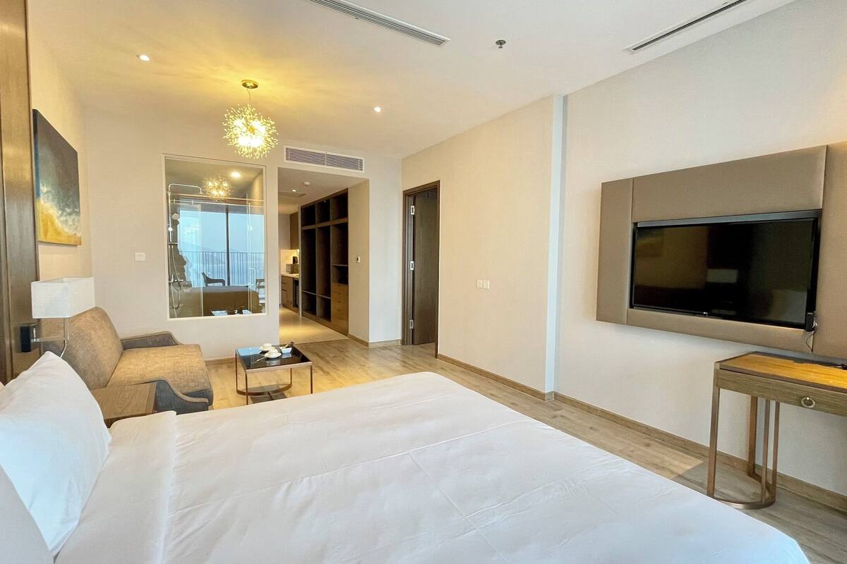 Una habitación de hotel con una cama grande, un televisor montado en la pared, un escritorio y un rincón de descanso con una mesa y sillas.