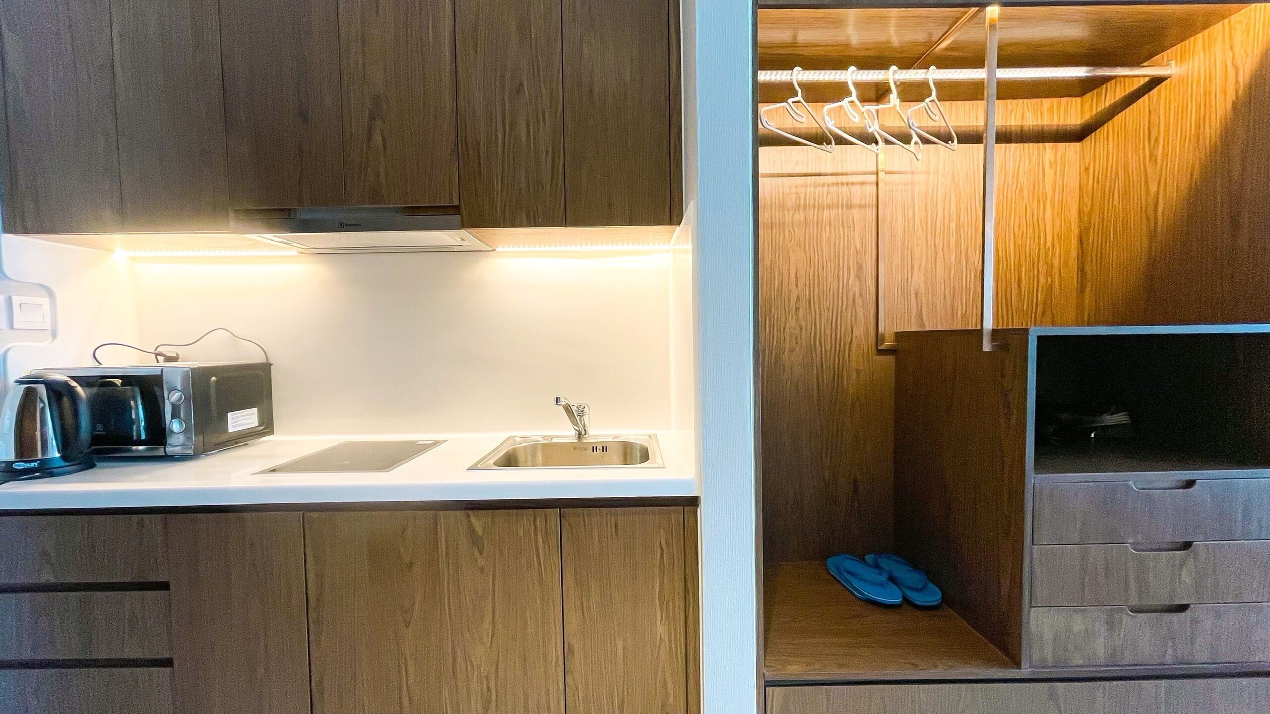 Une cuisine de taille réduite, dotée de meubles de rangement en bois, d’un évier, d’un grille-pain et d’une étagère suspendue.