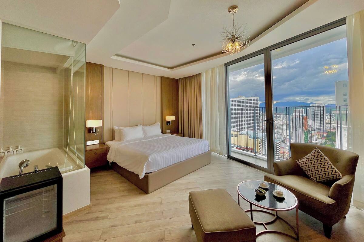 Habitación de hotel moderna con una cama grande, un sofá, una mesita y vistas de la ciudad.