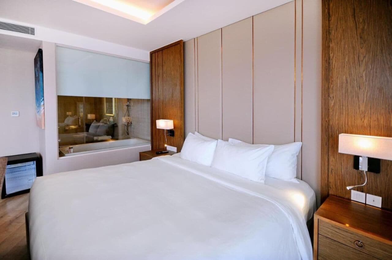 Una camera d'albergo moderna con un letto grande, pannelli in legno e un ampio specchio che riflette l'ambiente.