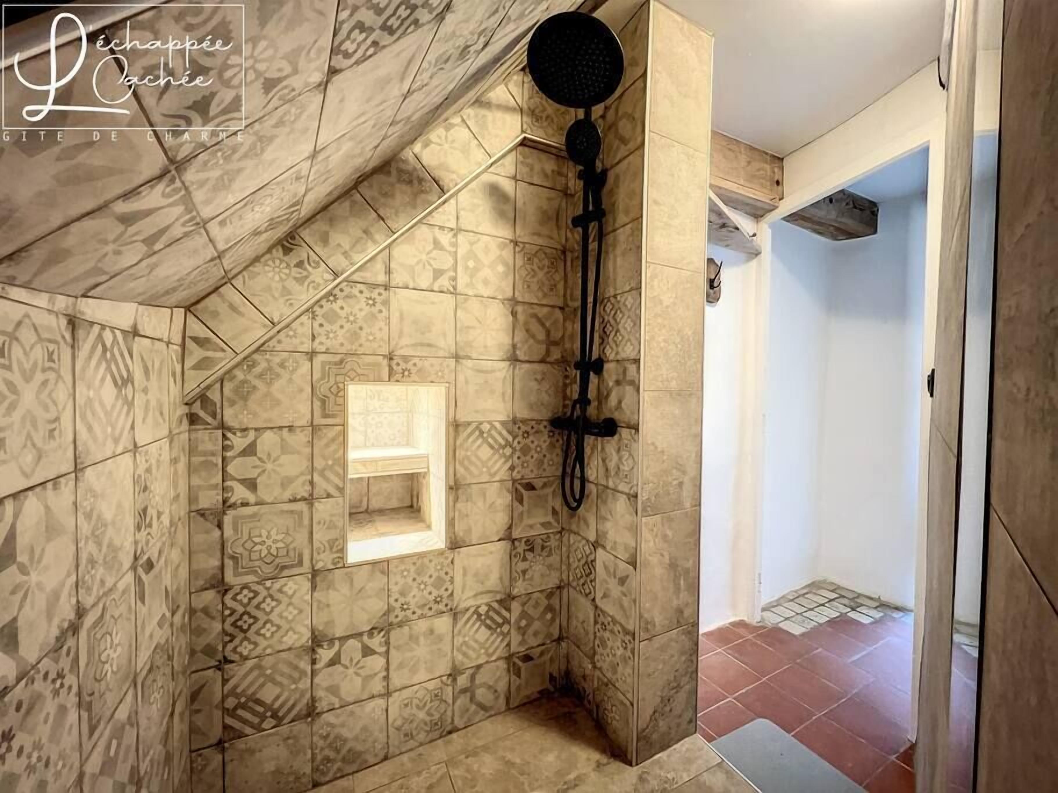 A shower area with patterned tiles, a showerhead, and a small shelf.