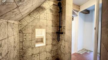 A shower area with patterned tiles, a showerhead, and a small shelf.