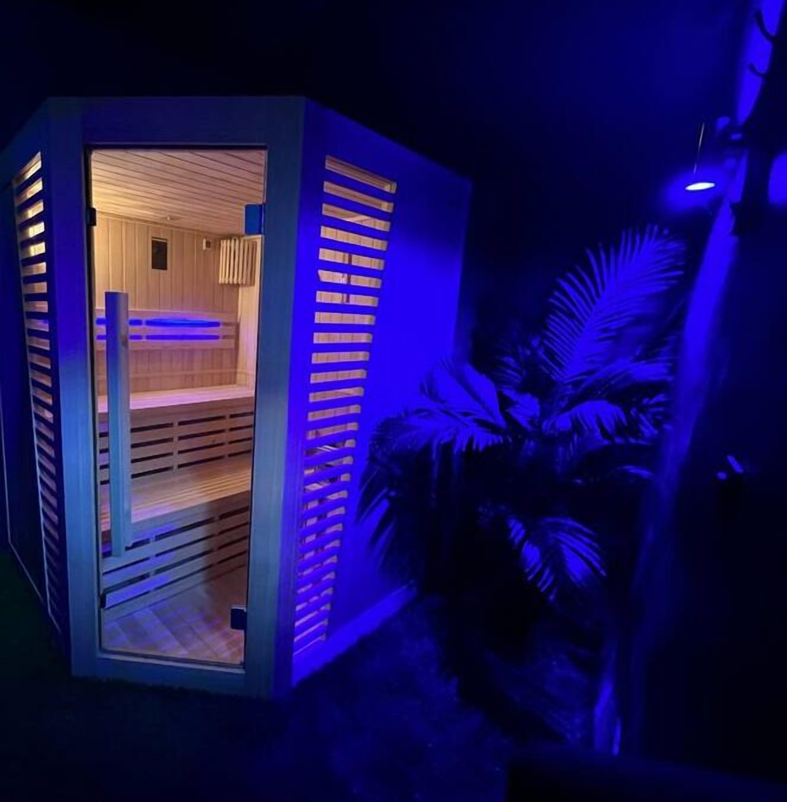A sauna with wooden benches and a slatted door, illuminated by blue lighting.