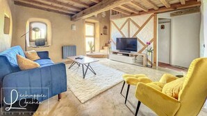 Un salón espacioso con un sofá azul, sillones amarillos, un televisor sobre un mueble de madera y un techo rústico.