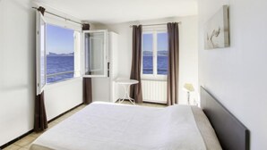 Ein Hotelzimmer mit Bett, einem Fenster mit Vorhängen, einem kleinen Tisch und einem Bild an der Wand.