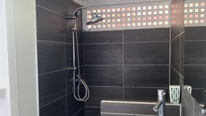 A modern bathroom with dark tiles, a shower, and a wooden vanity.
