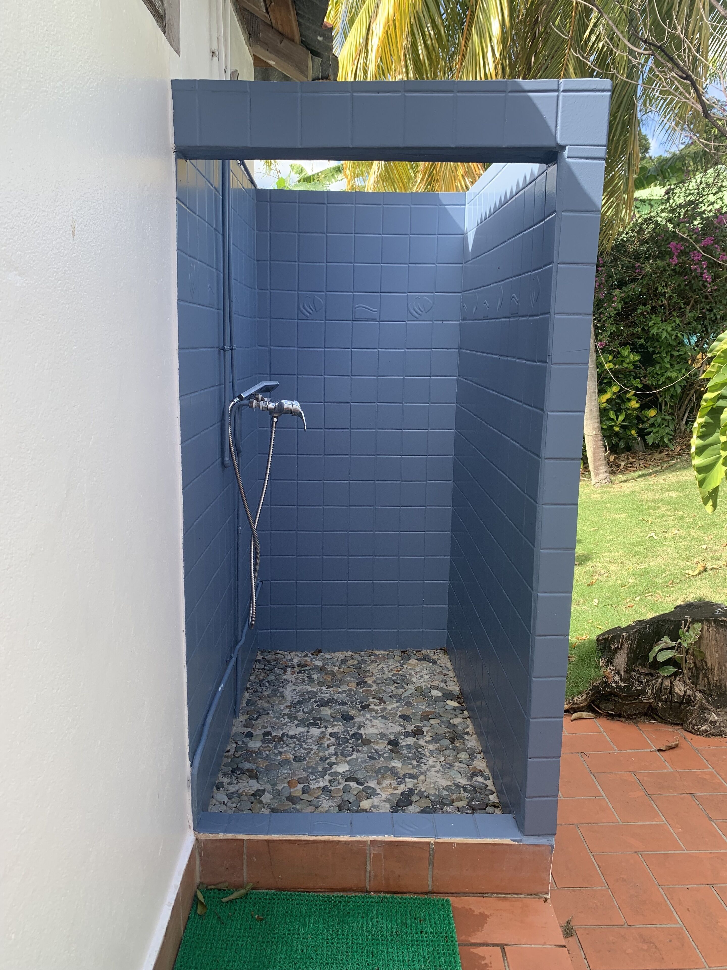 A small, enclosed shower area with a tiled blue interior and a green mat at the entrance.