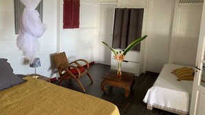 A room with a bed, a chair, a small table, a mirror, and a window with curtains.
