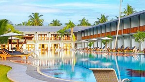 A hotel with a swimming pool, sun loungers, and a covered area with umbrellas.