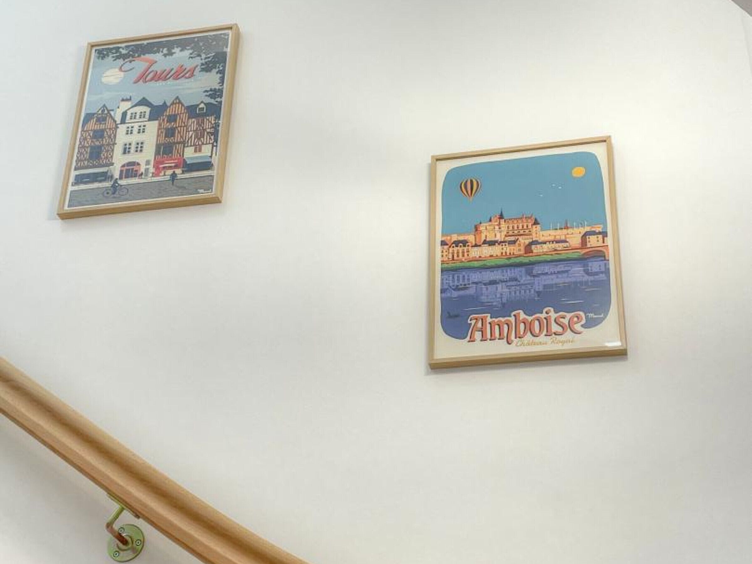 Two framed posters on a wall, one depicting a town scene and the other a cityscape with a hot air balloon.