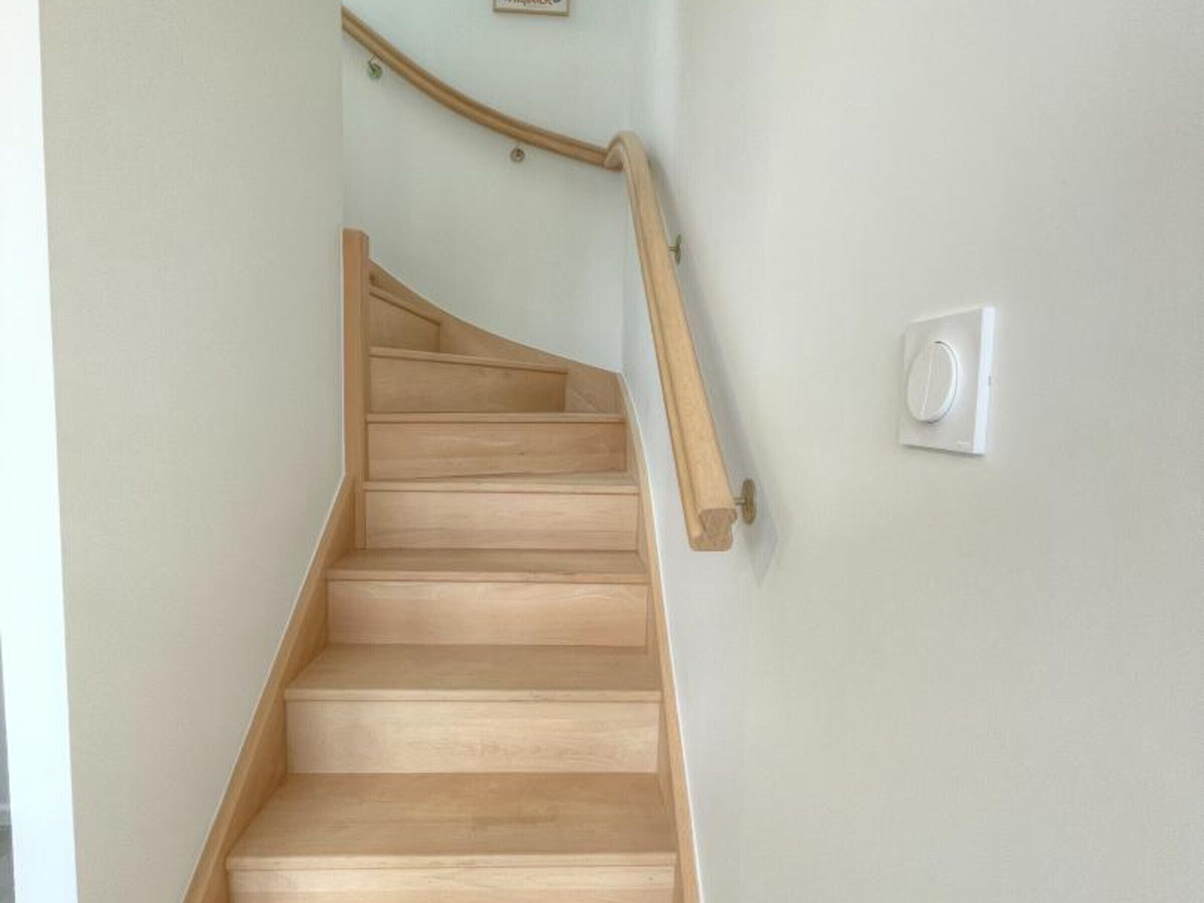 A wooden staircase with a handrail and a light switch on the wall.