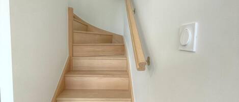 A wooden staircase with a handrail and a light switch on the wall.