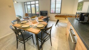 A dining area with a wooden table set for four, surrounded by chairs. There is a foosball table to the right and a kitchen area with a coffee machine. - Charming Gîte with Private Pool near Amboise, Sleeps 5, Fully Equipped (Saint-Règle)