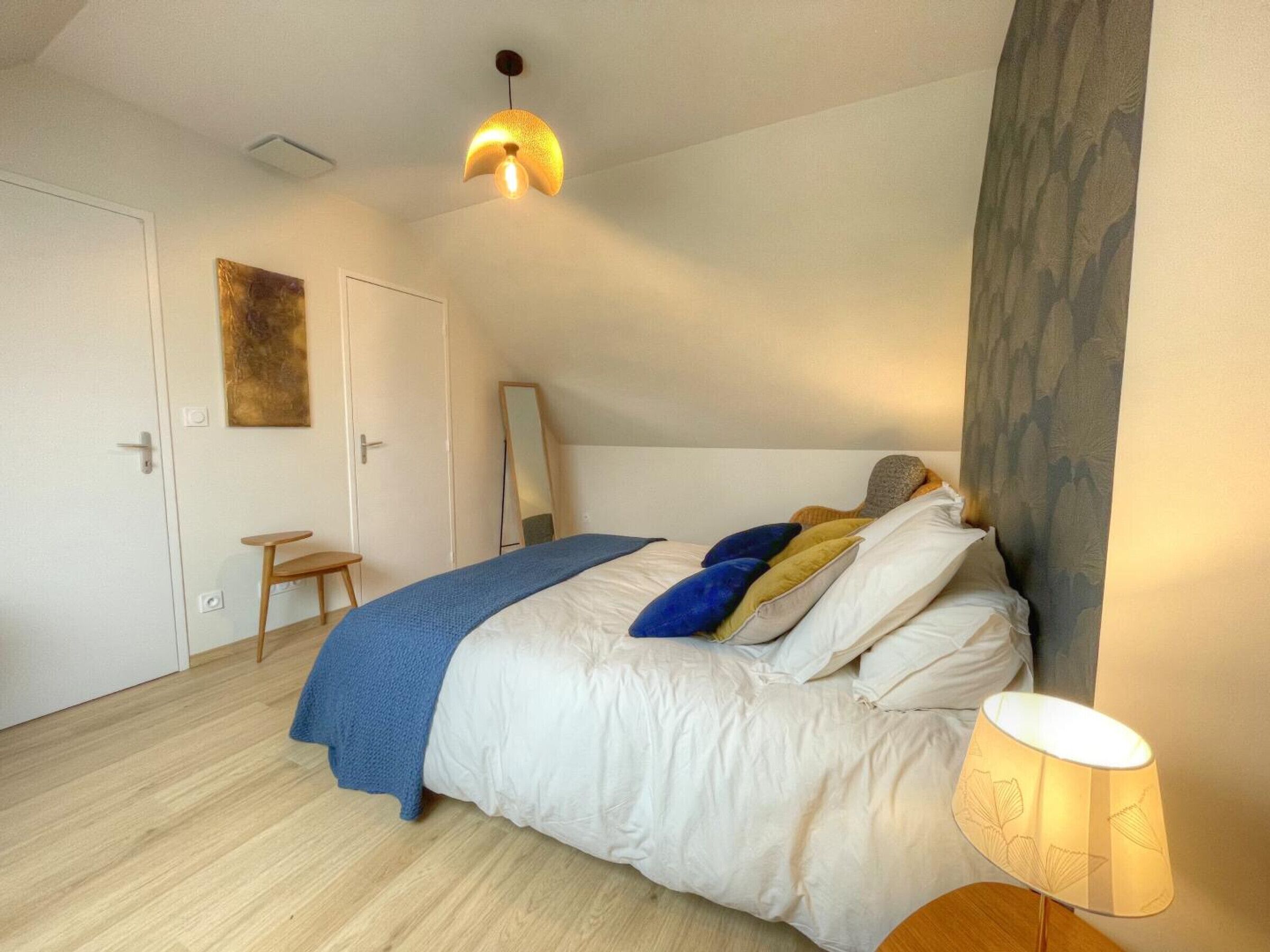 A bedroom with a bed, a bedside lamp, a mirror, and a door.