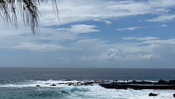 Ein Strand mit brechenden Wellen, einem klaren Himmel und Felsen in der Ferne.
