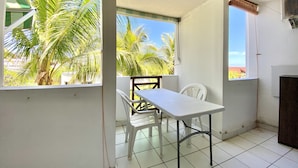 Ein Balkon mit weißem Tisch und Stühlen, der auf Palmen und einen klaren Himmel blickt.