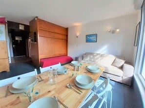 Ein gemütlicher Wohnbereich mit Esstisch für vier Personen, einer Couch und einem Holzschrank mit rotem Kissen.