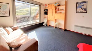 A room with a large window, a wooden cabinet, a white stool, and a red chair. - Spacious 6-Person Studio with Bunk Beds and Ski Locker, Dishwasher, and Fondue Set (Piau-Engaly)