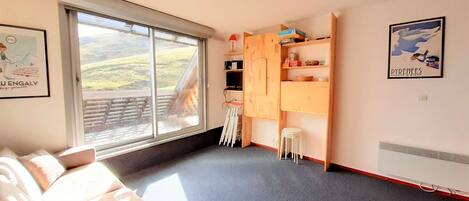 A room with a large window, a wooden cabinet, a white stool, and a red chair.