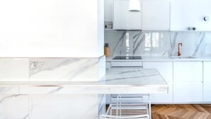A modern kitchen with white cabinetry, marble countertops, a built-in oven, and a pendant light. - Molière Design residence  (Brussels)