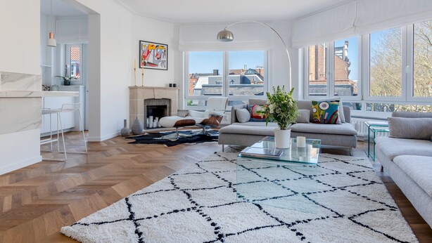 A modern living room with a fireplace, a sofa, a coffee table, and a view of the city through large windows. - Molière Design residence  (Brussels)