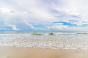 A beach with waves gently lapping onto the shore under a partly cloudy sky. - DUNES 102, 1/2 1st Floor, No Elevator, Sea South Properties (Gulf Shores)