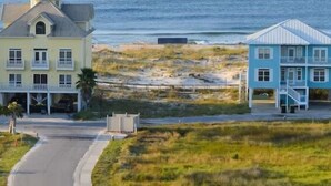 A coastal road leading to two beachfront buildings with balconies, one yellow and one blue, overlooking the ocean. - DUNES 102, 1/2 1st Floor, No Elevator, Sea South Properties (Gulf Shores)