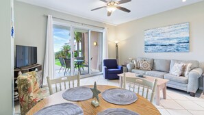 A living room with a sofa, a television, a ceiling fan, and a painting on the wall. - DUNES 102, 1/2 1st Floor, No Elevator, Sea South Properties (Gulf Shores)