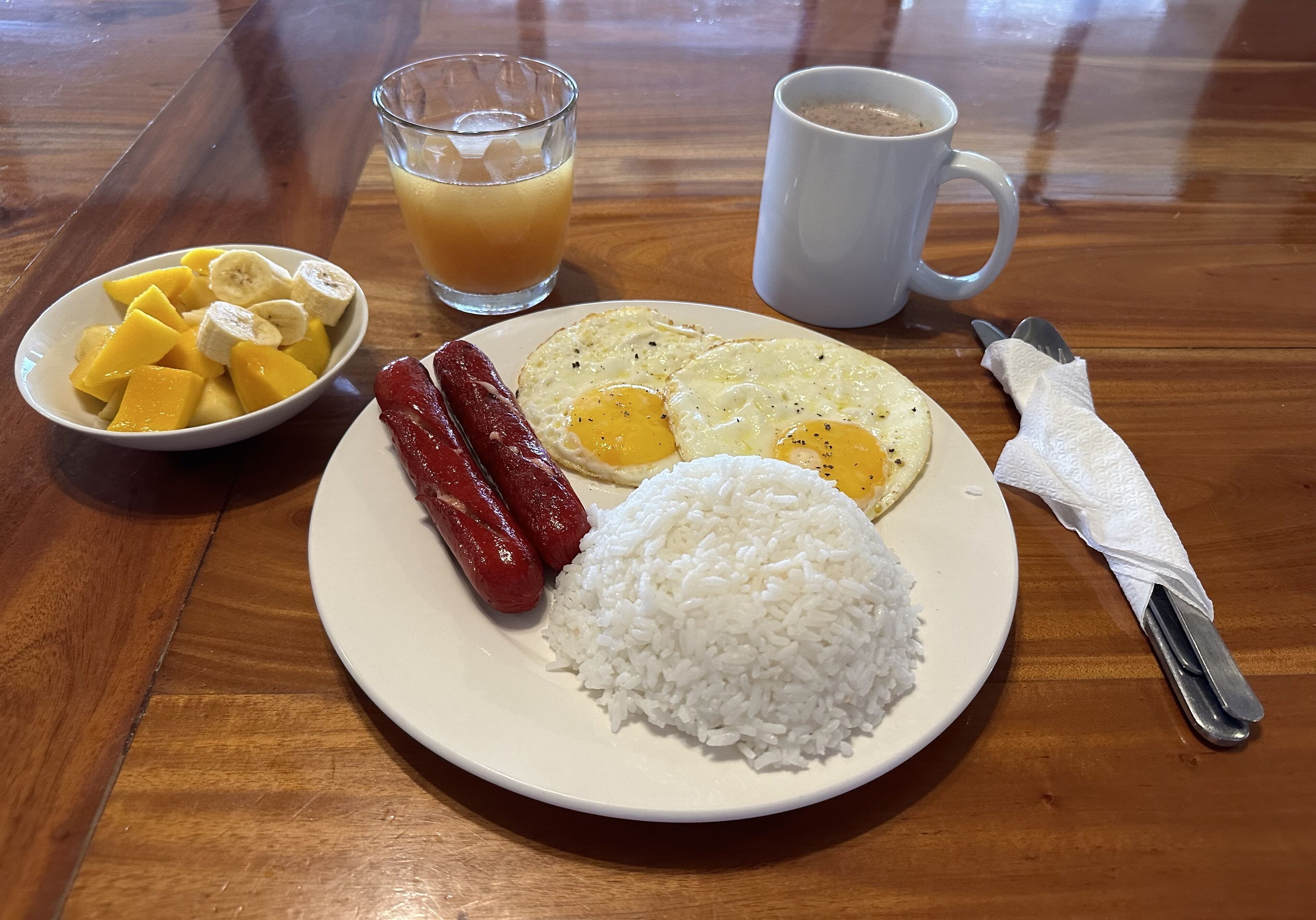 A plate with white rice, two fried eggs, and two sausages.