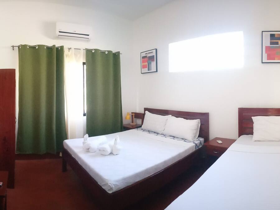 A hotel room with two beds, a TV, an air conditioner, and a window with curtains.