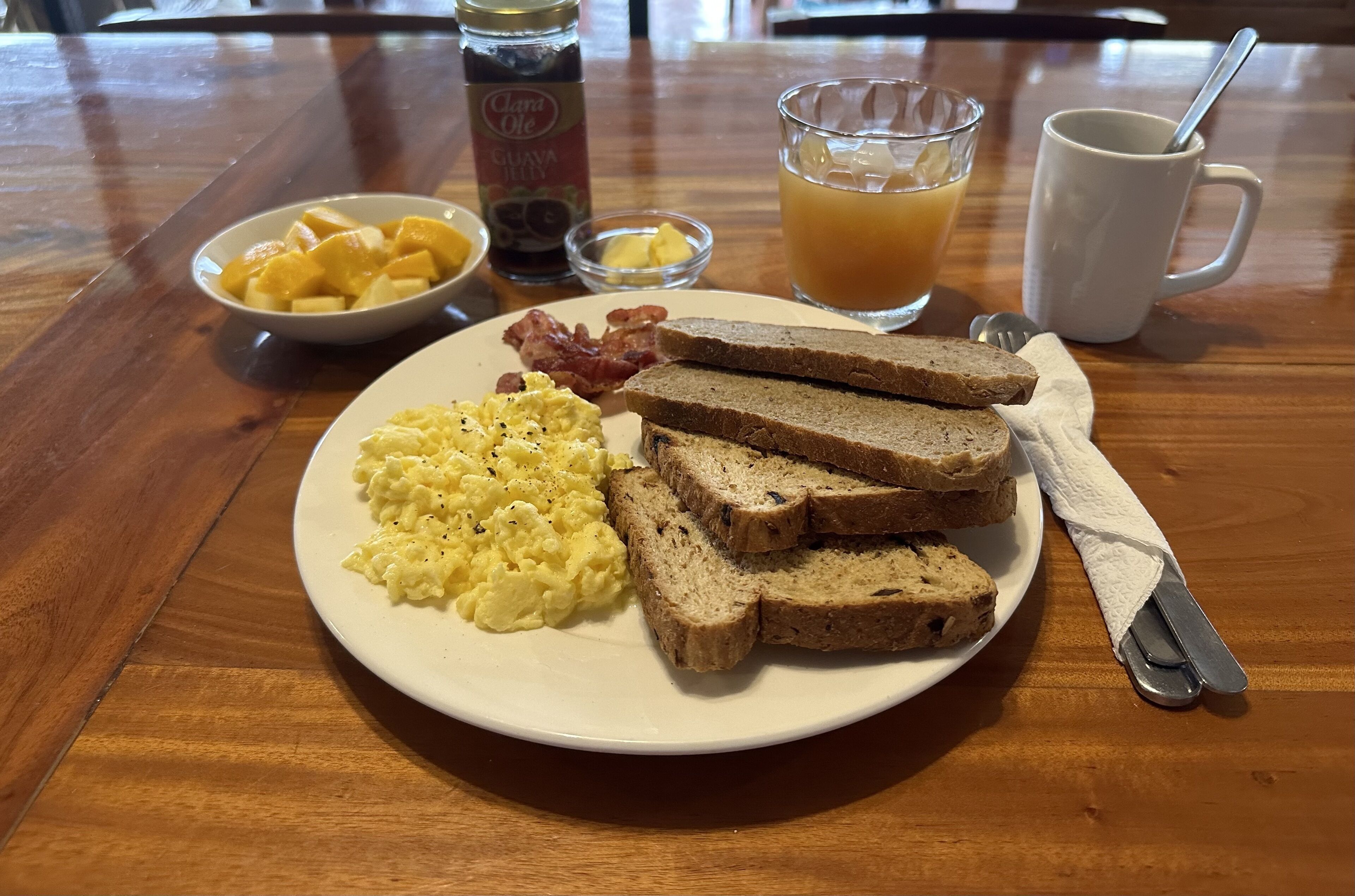 A breakfast plate with scrambled eggs, toast, bacon, and a glass of orange juice on a wooden table.