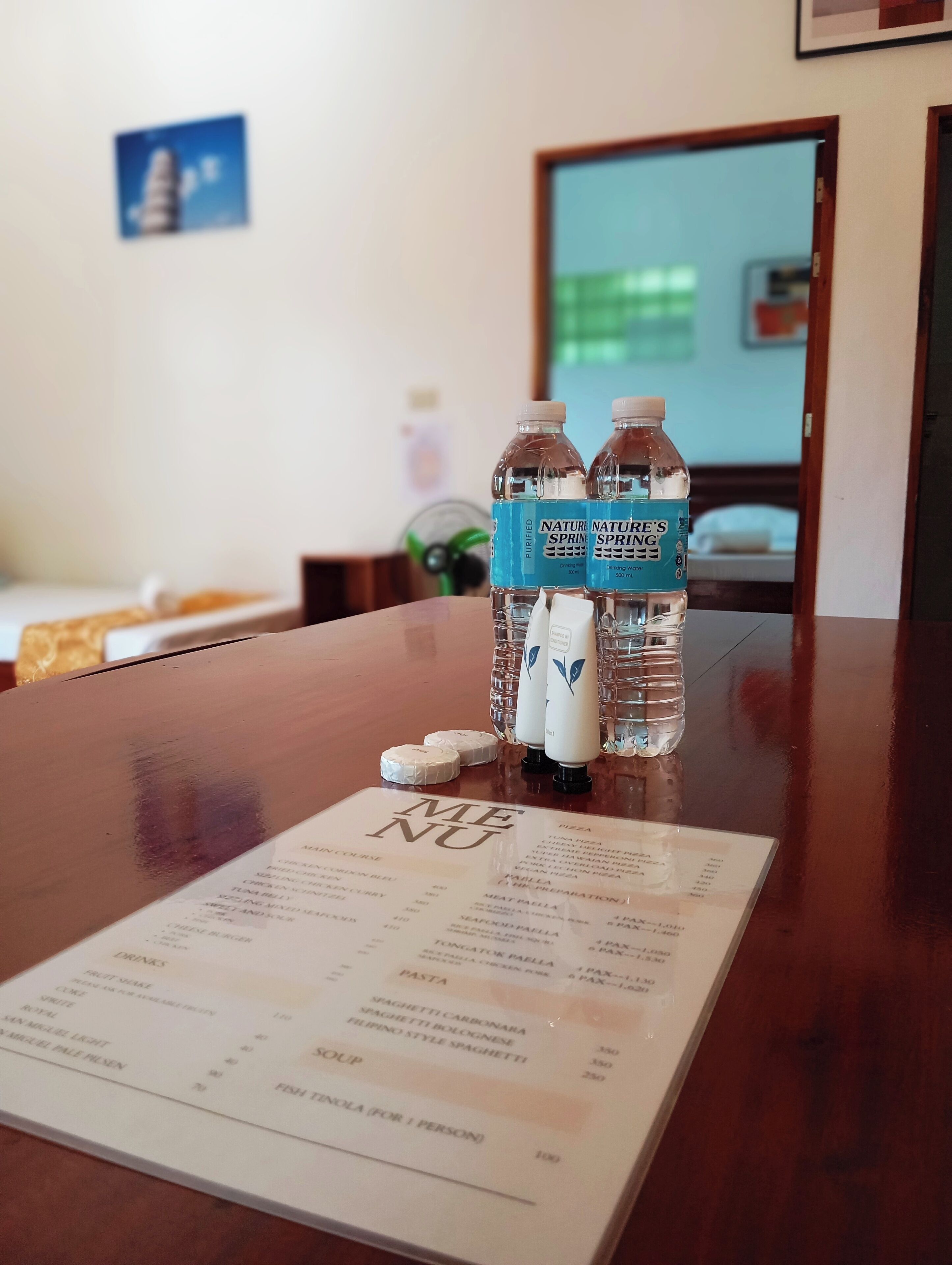 A menu on a wooden table with two Nature Spring water bottles and two white bottles with blue labels.
