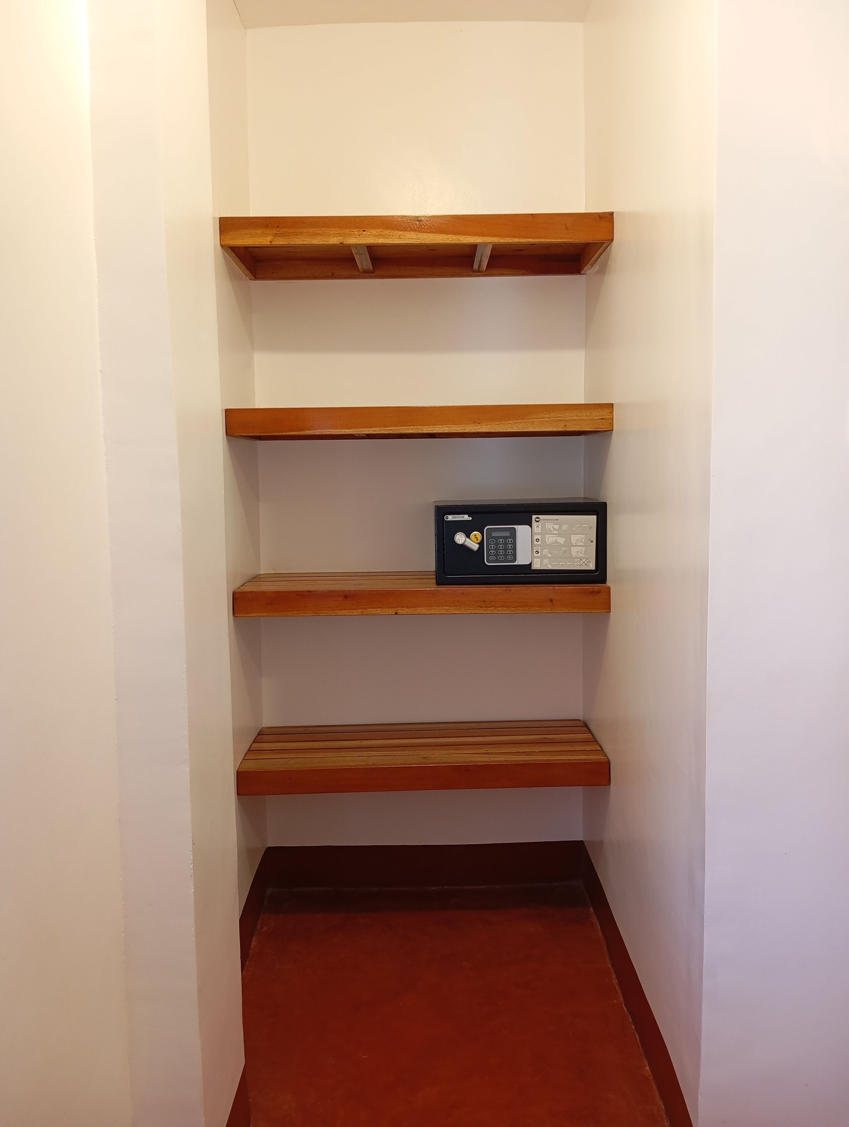 A hallway with three wooden shelves and a black security device on the middle shelf.
