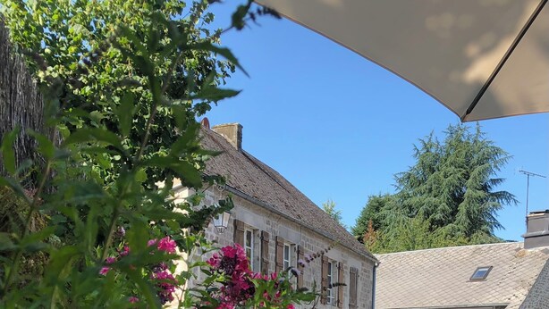 A stone building with a sloped roof, surrounded by greenery and flowering plants. - LA PETITE MAISON à TARNAC en CORRÈZE (Tarnac)