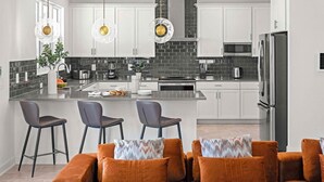 A modern kitchen with white cabinets, a black backsplash, stainless steel appliances, and a central island with bar stools. - Hi340sd: 5 Bed, Storybook Village, Karaoke (Melbourne Beach)