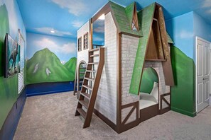 Uma casinha com escada e janela, com um mural ao fundo mostrando colinas verdes e céu azul.