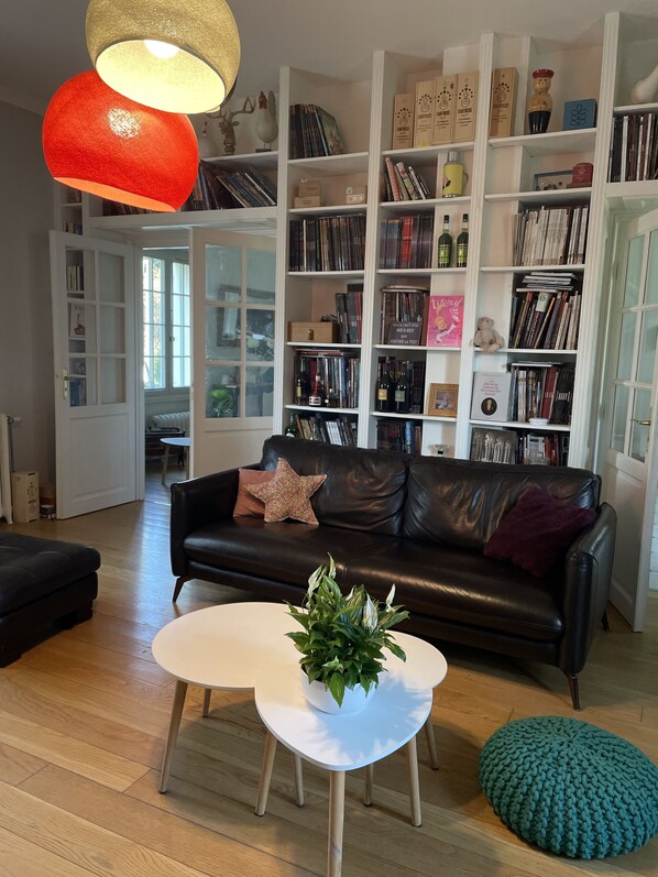 A living room with a black leather sofa, a white coffee table with a plant, and a bookshelf filled with books and decorative items.