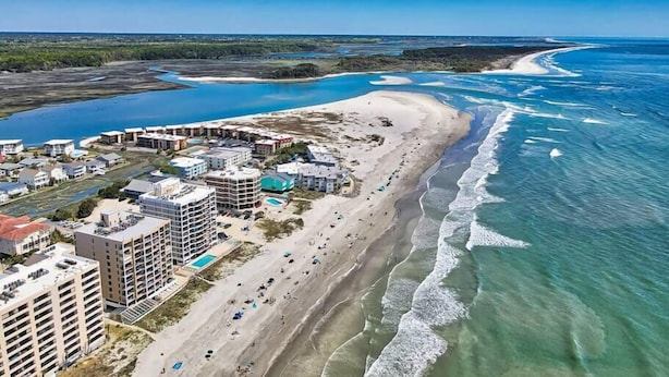 A coastal resort with beachfront properties, a marina, and a beach with people.