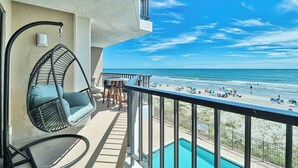 A balcony with a hanging chair, a pool, and a view of the beach.