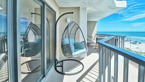 A balcony with a hanging chair and a table, overlooking a beach.