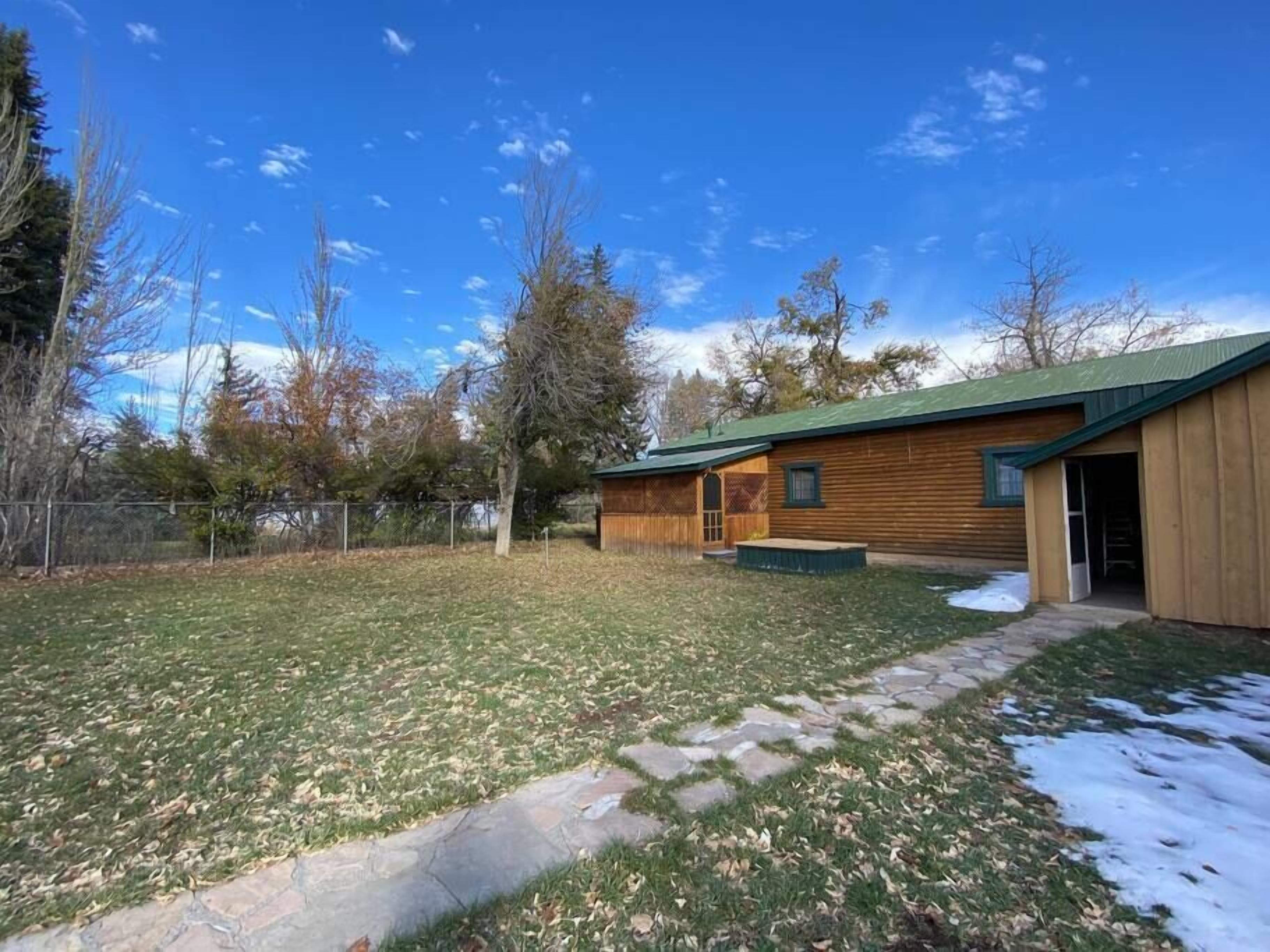 Una cabaña de madera con techo verde, un camino de piedra y un patio cercado.