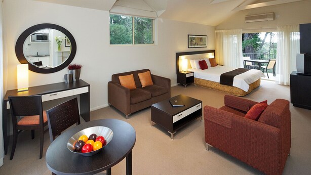 Une chambre d’hôtel comprenant un lit, deux canapés, une table à manger avec des fruits, un bureau avec un miroir et une télévision.