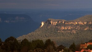 Un paysage montagneux caractérisé par une falaise imposante et une maison avec un toit rouge située au pied de celle-ci.