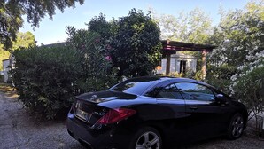 En sort bil parkeret på en grusvej med en pergola og frodig beplantning i baggrunden.