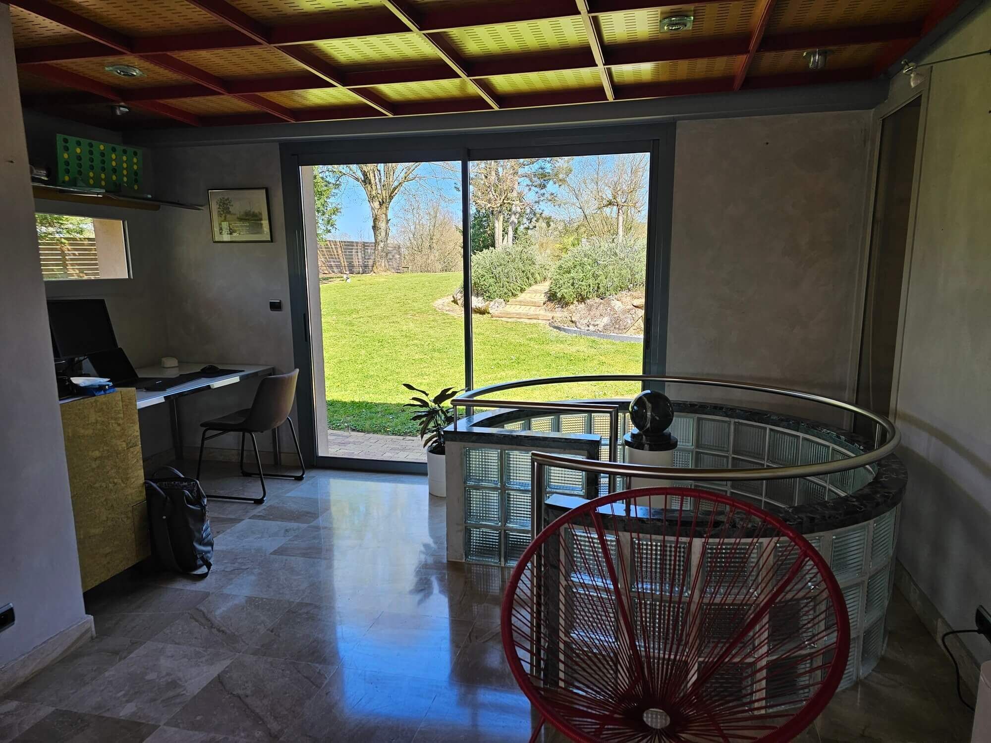 Un interior moderno con un escritorio, computadora y vista a un jardín césped a través de una puerta de vidrio.