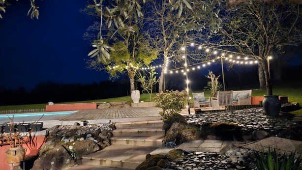 A nighttime outdoor patio area with string lights, a pool, and a seating area with chairs and a table.