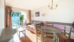 Ein Wohnzimmer mit einer Couch, einem Esstisch mit Stühlen, einem Fernseher und einer Pendelleuchte.