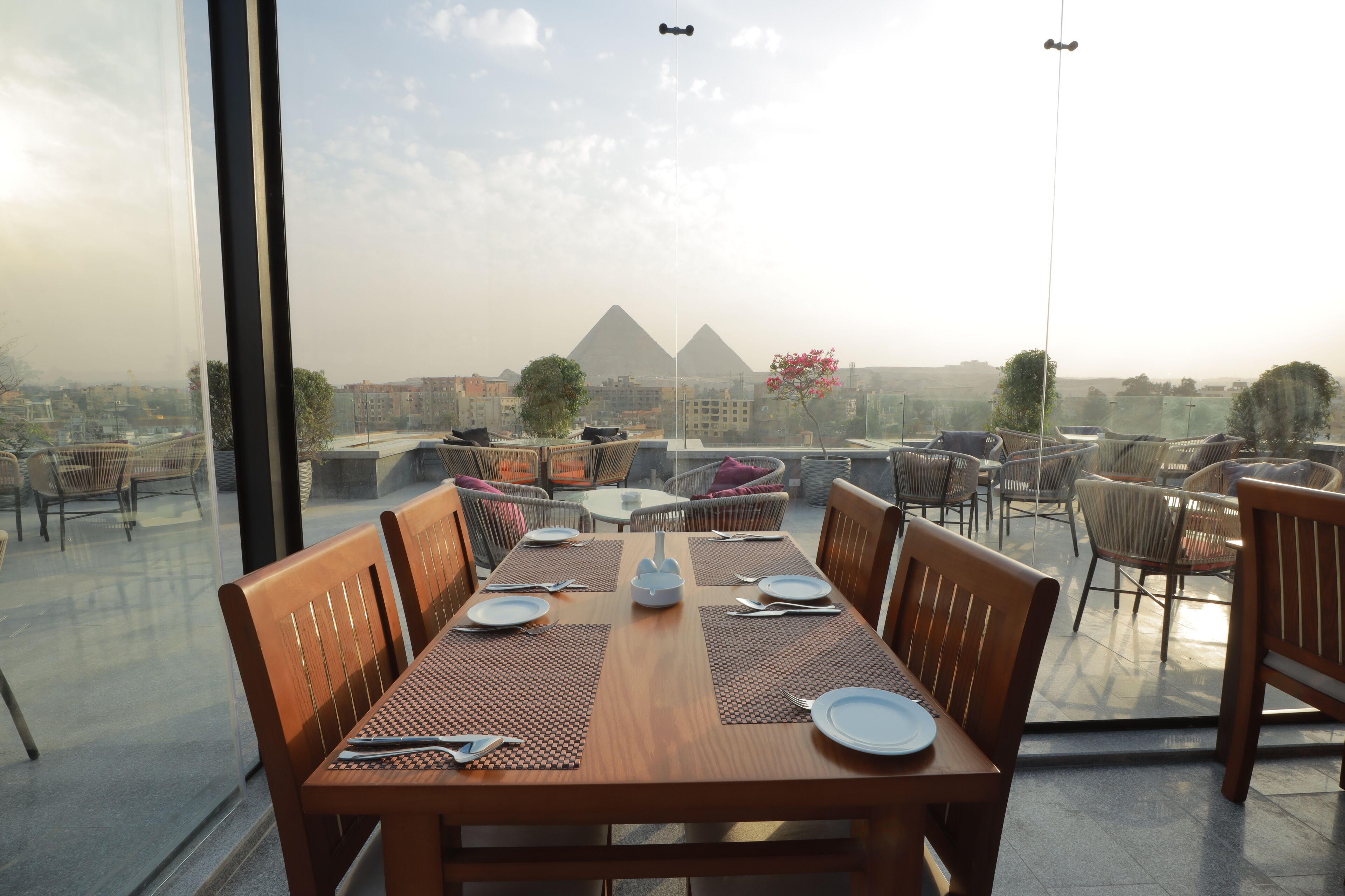 A dining area with a view of the pyramids, equipped with wooden tables and chairs, and a clear glass partition.