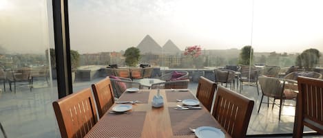 A dining area with a view of the pyramids, equipped with wooden tables and chairs, and a clear glass partition.